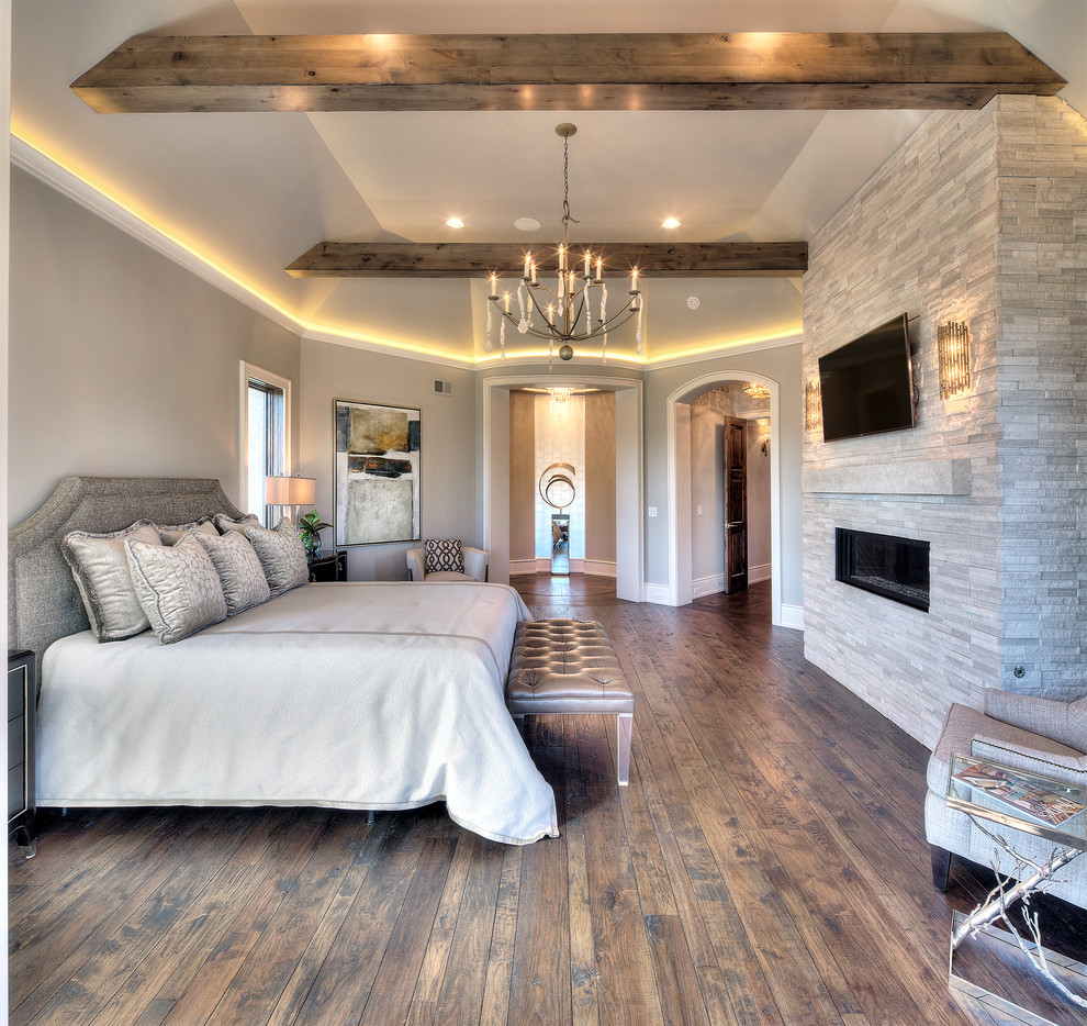 Cette image montre une chambre parentale design avec un mur gris, un sol en bois brun, une cheminée ribbon et un manteau de cheminée en pierre.