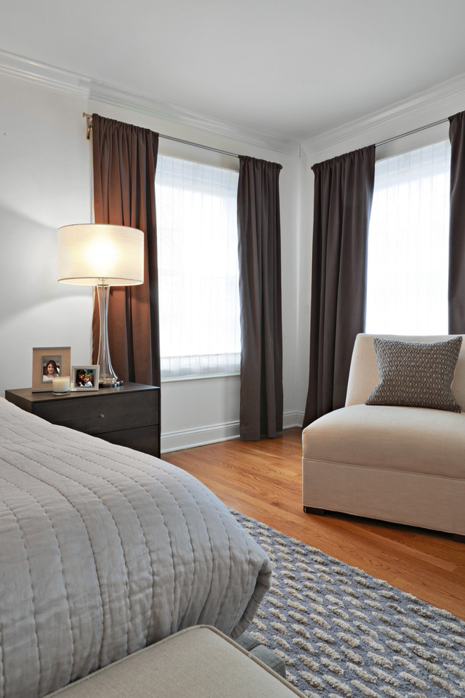 This is an example of a medium sized modern grey and cream and master bedroom in New York with white walls, light hardwood flooring and brown floors.