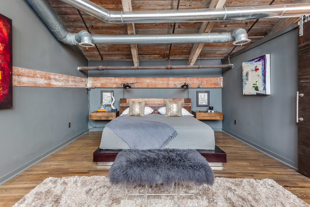 Foto di una camera da letto industriale con pareti grigie e pavimento in legno massello medio