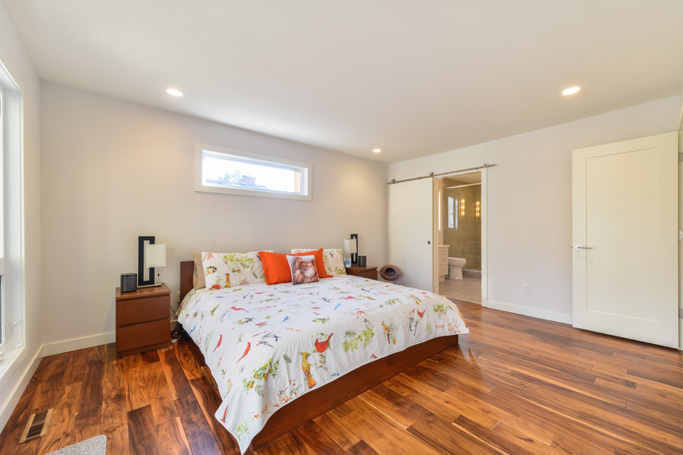 Modelo de dormitorio principal contemporáneo de tamaño medio sin chimenea con paredes grises, suelo de madera en tonos medios y suelo marrón