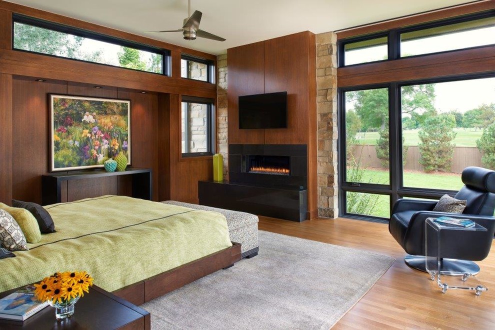 Inspiration pour une grande chambre parentale design avec un sol en bois brun, une cheminée ribbon et un manteau de cheminée en pierre.