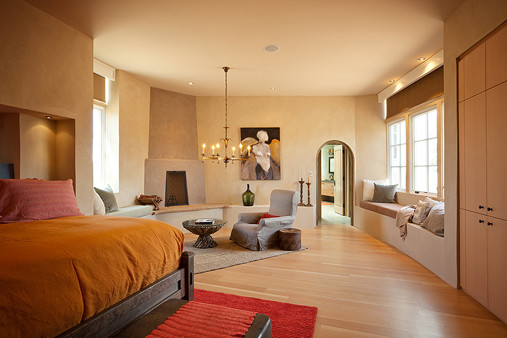 Modelo de dormitorio principal actual de tamaño medio con paredes beige, suelo de madera clara, chimenea de esquina y marco de chimenea de hormigón