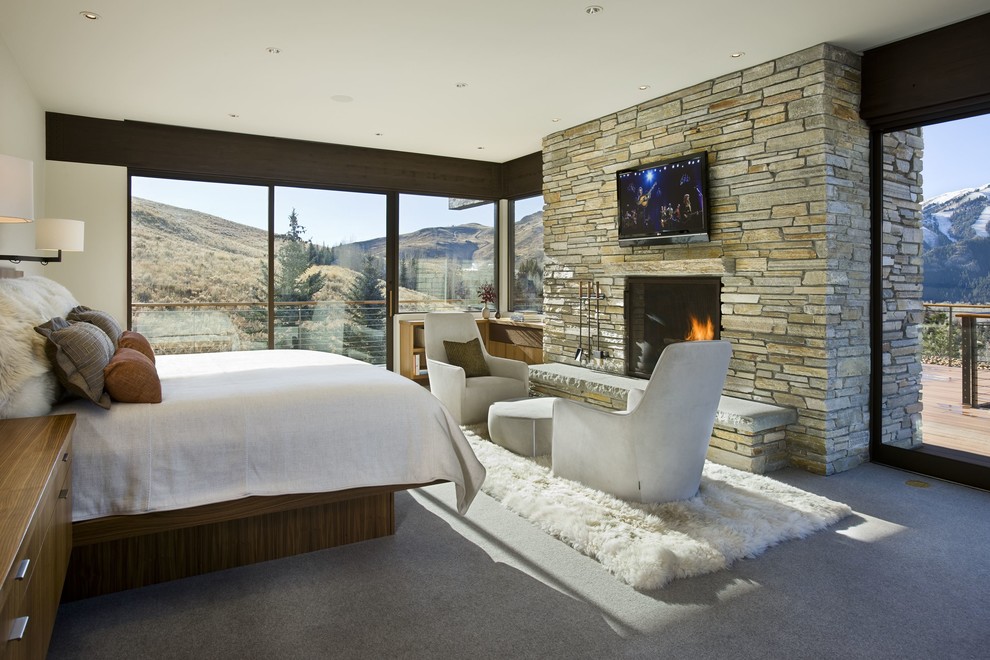 Modelo de dormitorio televisión actual con paredes blancas, moqueta, todas las chimeneas y marco de chimenea de piedra