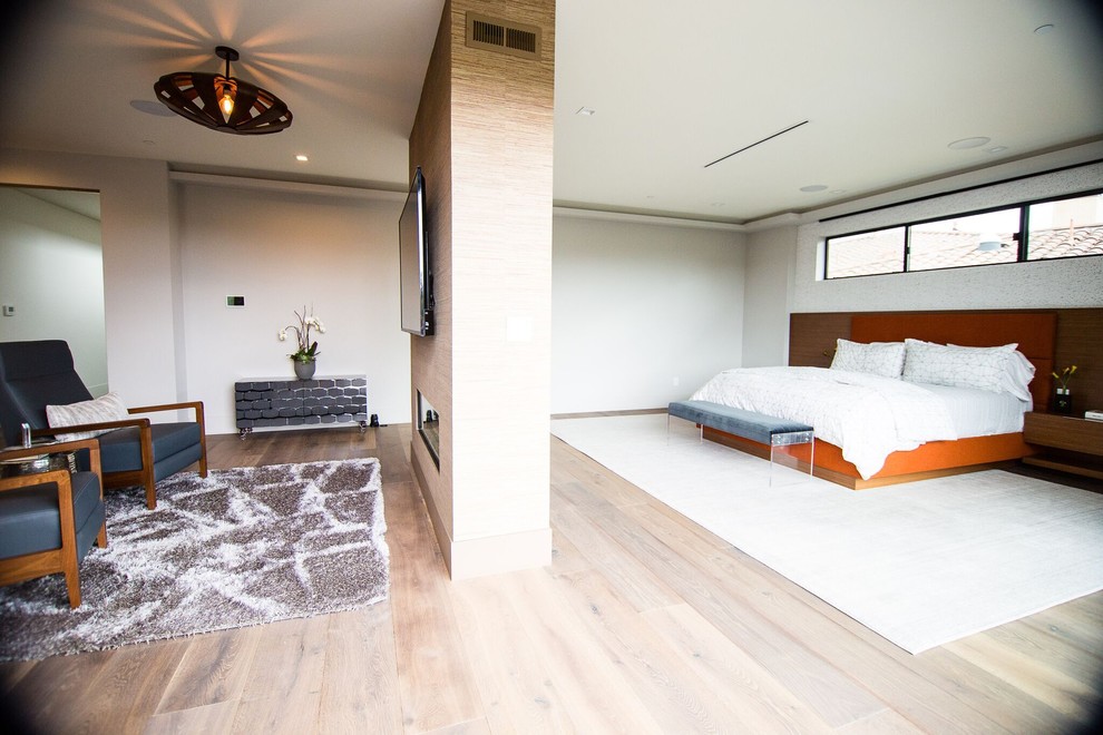 На фото: огромная хозяйская спальня в современном стиле с серыми стенами, паркетным полом среднего тона, двусторонним камином и серым полом с