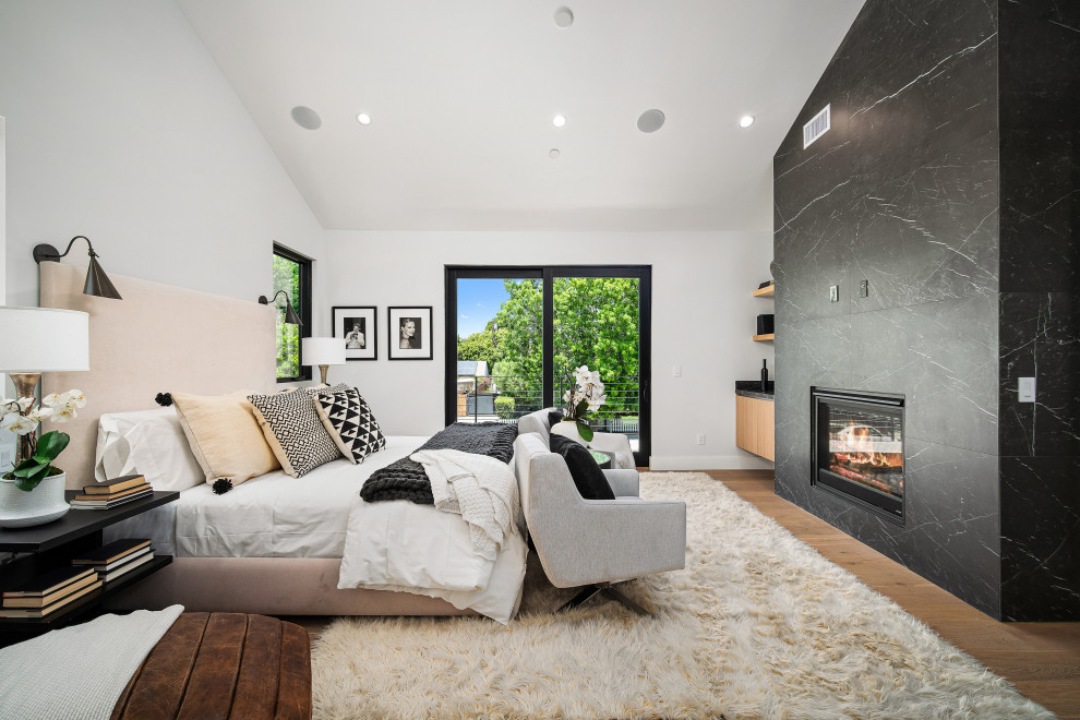 Modernes Schlafzimmer mit weißer Wandfarbe, braunem Holzboden, Kamin, Kaminumrandung aus Stein und braunem Boden in Los Angeles