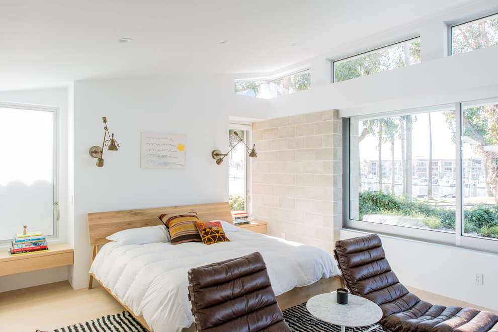 Diseño de dormitorio costero sin chimenea con paredes blancas, suelo de madera clara y suelo beige