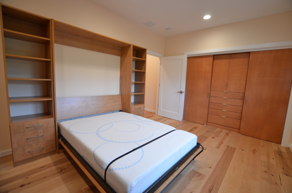 Ejemplo de habitación de invitados actual de tamaño medio con paredes amarillas y suelo de madera clara
