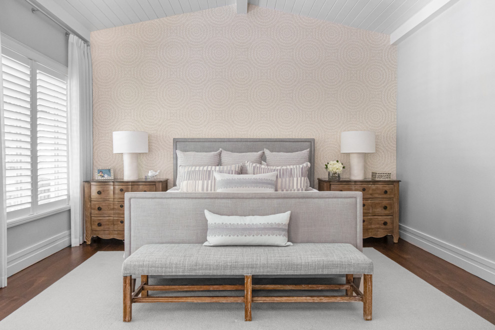 Modelo de dormitorio abovedado tradicional renovado con paredes beige, suelo de madera oscura, suelo marrón, machihembrado y papel pintado