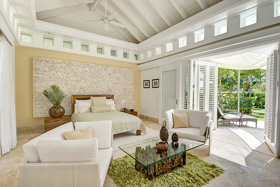 Modelo de dormitorio principal tropical grande sin chimenea con paredes beige, suelo de travertino y suelo marrón