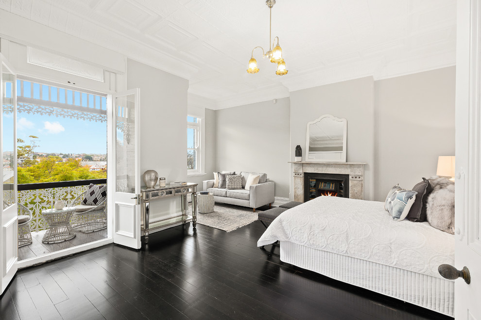 シドニーにある中くらいなトランジショナルスタイルのおしゃれな主寝室 (グレーの壁、標準型暖炉、石材の暖炉まわり、黒い床、塗装フローリング)