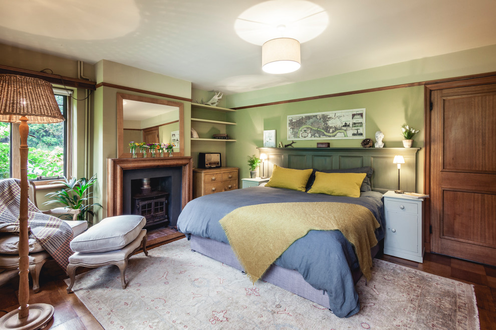 Idéer för mellanstora lantliga sovrum, med gröna väggar, mörkt trägolv, en öppen vedspis och brunt golv