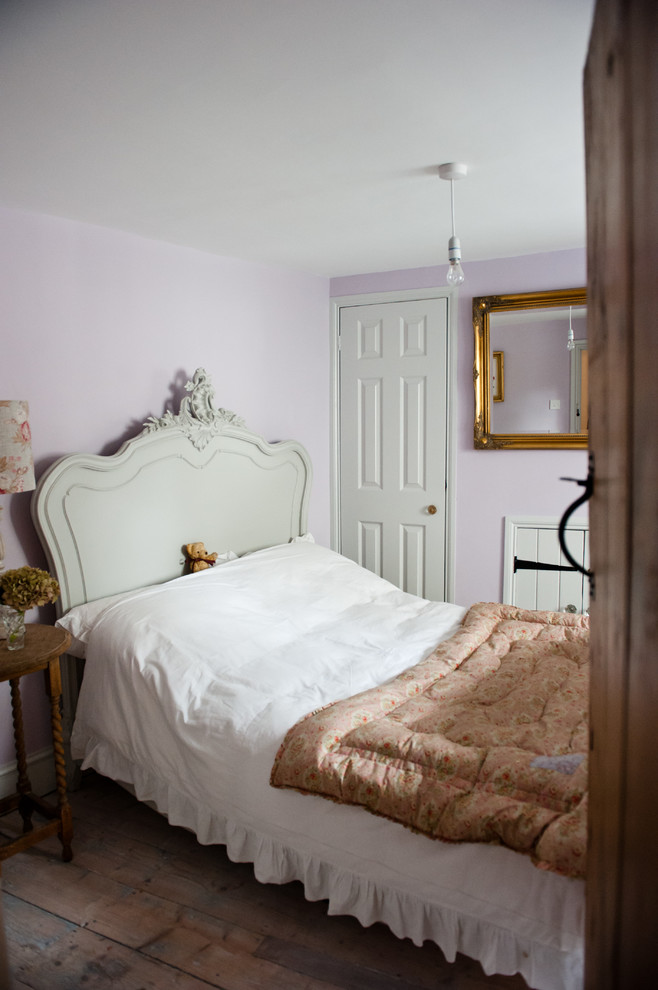 Ejemplo de habitación de invitados campestre pequeña con paredes púrpuras, suelo de madera clara y marco de chimenea de piedra