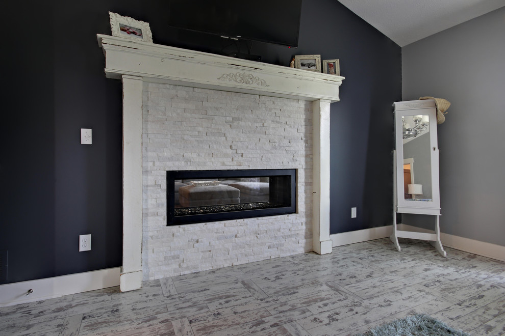Example of a large mountain style master laminate floor and white floor bedroom design in Grand Rapids with gray walls and a two-sided fireplace