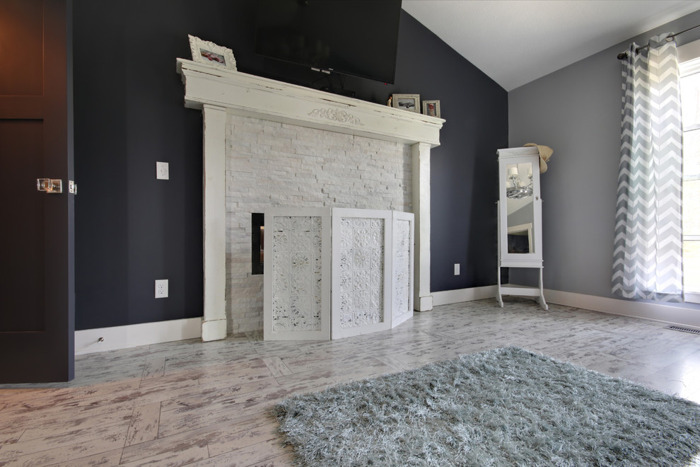 Photo of a large rustic master bedroom in Grand Rapids with grey walls, laminate floors, a two-sided fireplace, a stone fireplace surround and white floors.