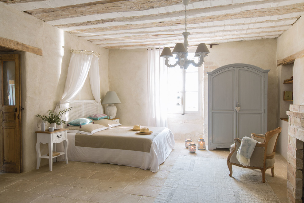 Esempio di una camera da letto mediterranea di medie dimensioni con pareti beige, pavimento in travertino, camino classico, cornice del camino in mattoni e pavimento beige