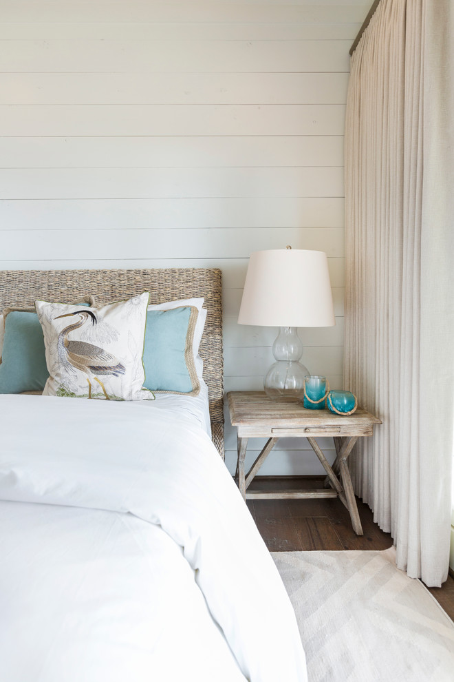 This is an example of a beach style master bedroom in Houston with white walls, dark hardwood flooring and feature lighting.