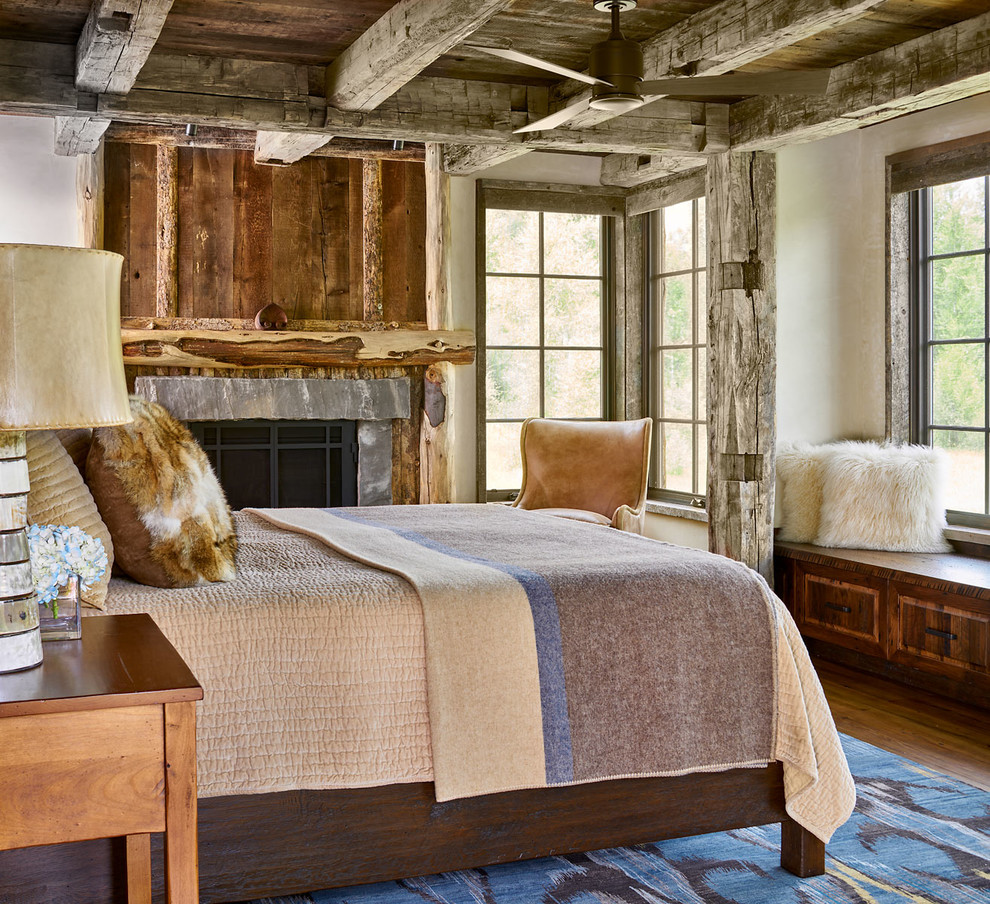 Modelo de dormitorio principal rural con paredes blancas, suelo de madera en tonos medios, todas las chimeneas, suelo marrón y marco de chimenea de piedra
