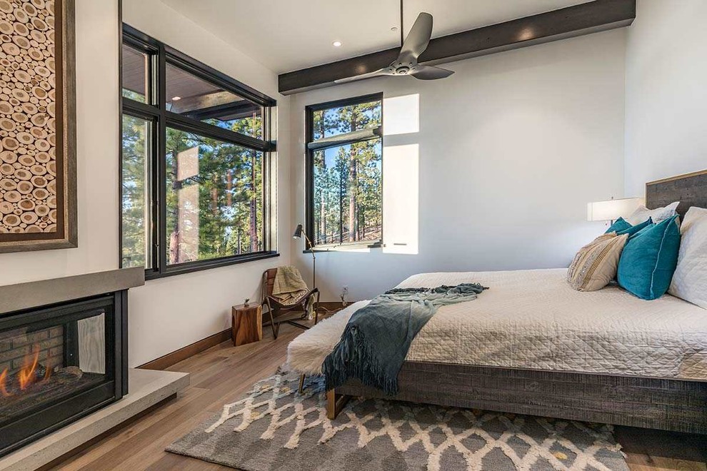 Diseño de habitación de invitados moderna sin chimenea con suelo de madera clara, marco de chimenea de hormigón y suelo marrón