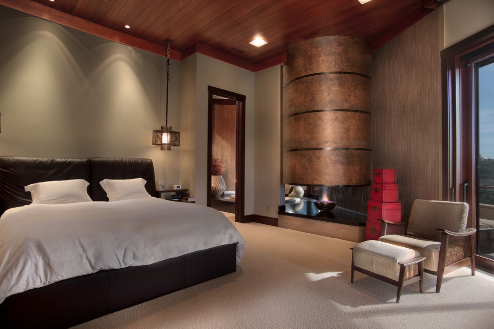 Imagen de dormitorio principal de estilo zen de tamaño medio con paredes beige, moqueta, chimenea de doble cara, marco de chimenea de metal y suelo beige