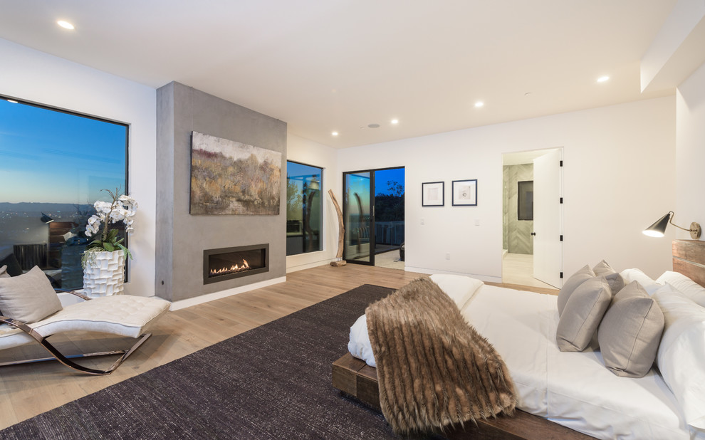 Großes Modernes Hauptschlafzimmer mit weißer Wandfarbe, hellem Holzboden, Gaskamin und Kaminumrandung aus Beton in Los Angeles
