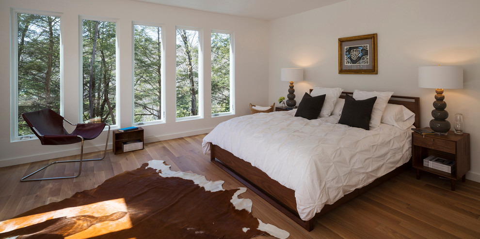 This is an example of a contemporary bedroom in New York with white walls and dark hardwood flooring.