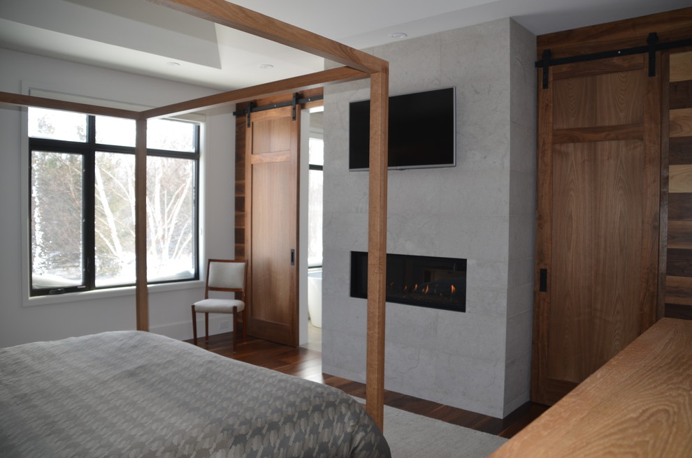 Diseño de dormitorio principal contemporáneo con paredes blancas, suelo de madera en tonos medios, todas las chimeneas y marco de chimenea de piedra