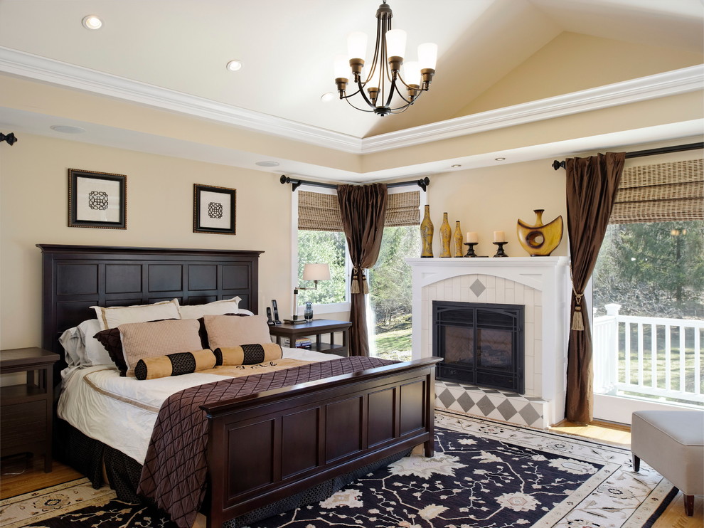 Modelo de dormitorio clásico con paredes beige, suelo de madera en tonos medios, todas las chimeneas y marco de chimenea de baldosas y/o azulejos