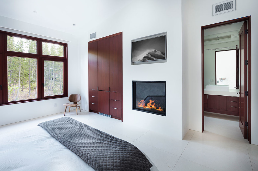Cette photo montre une grande chambre parentale tendance avec un mur blanc, une cheminée standard, un manteau de cheminée en plâtre et un sol blanc.