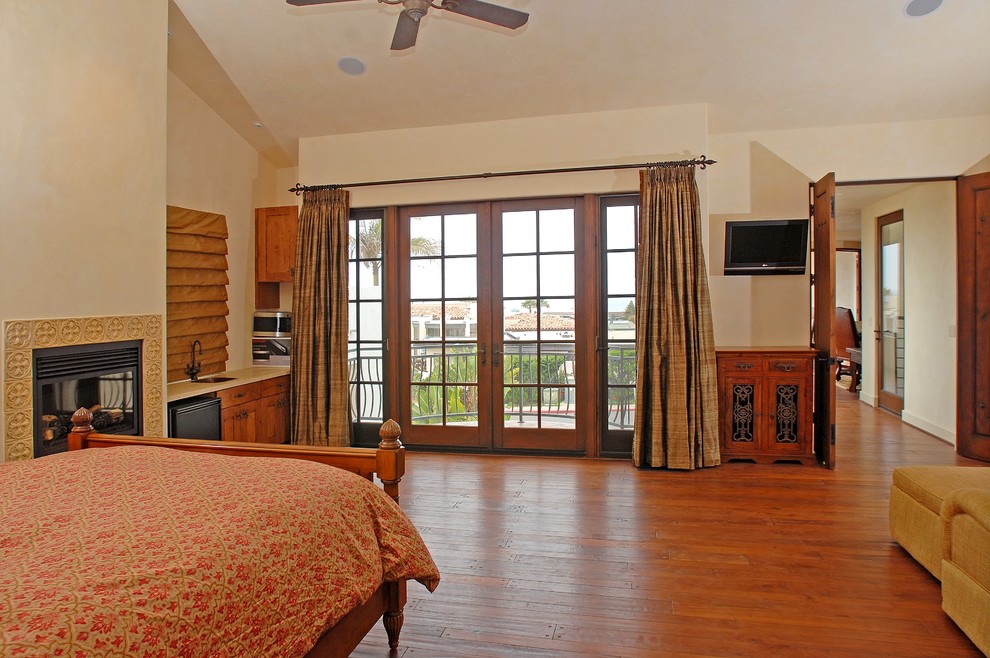 Großes Mediterranes Hauptschlafzimmer mit beiger Wandfarbe, braunem Holzboden, Hängekamin, gefliester Kaminumrandung und braunem Boden in San Diego