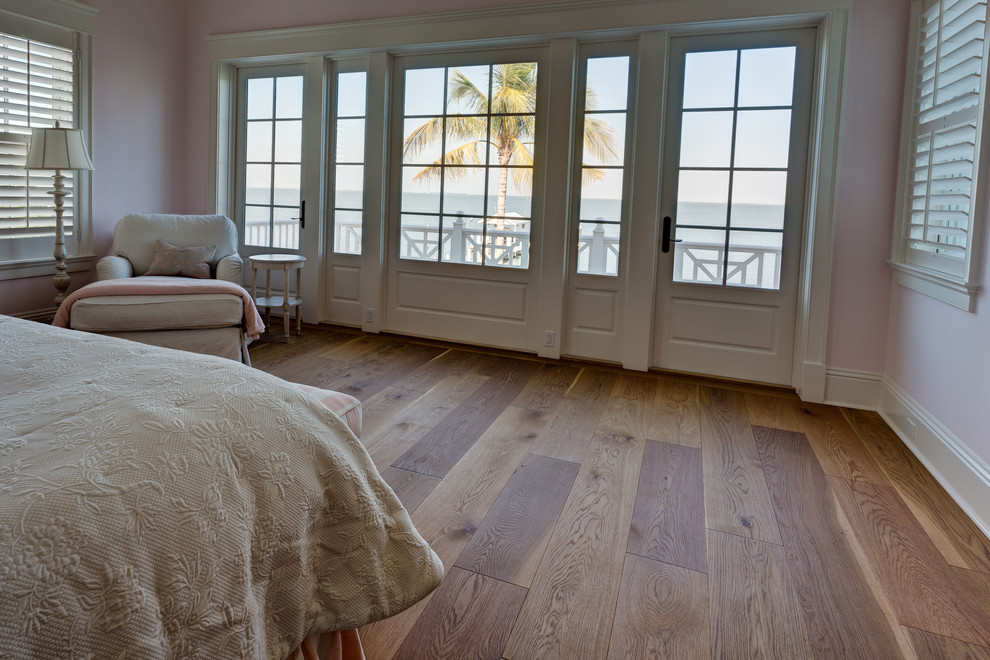 Imagen de dormitorio principal de estilo americano de tamaño medio sin chimenea con suelo de madera en tonos medios, paredes rosas y suelo marrón