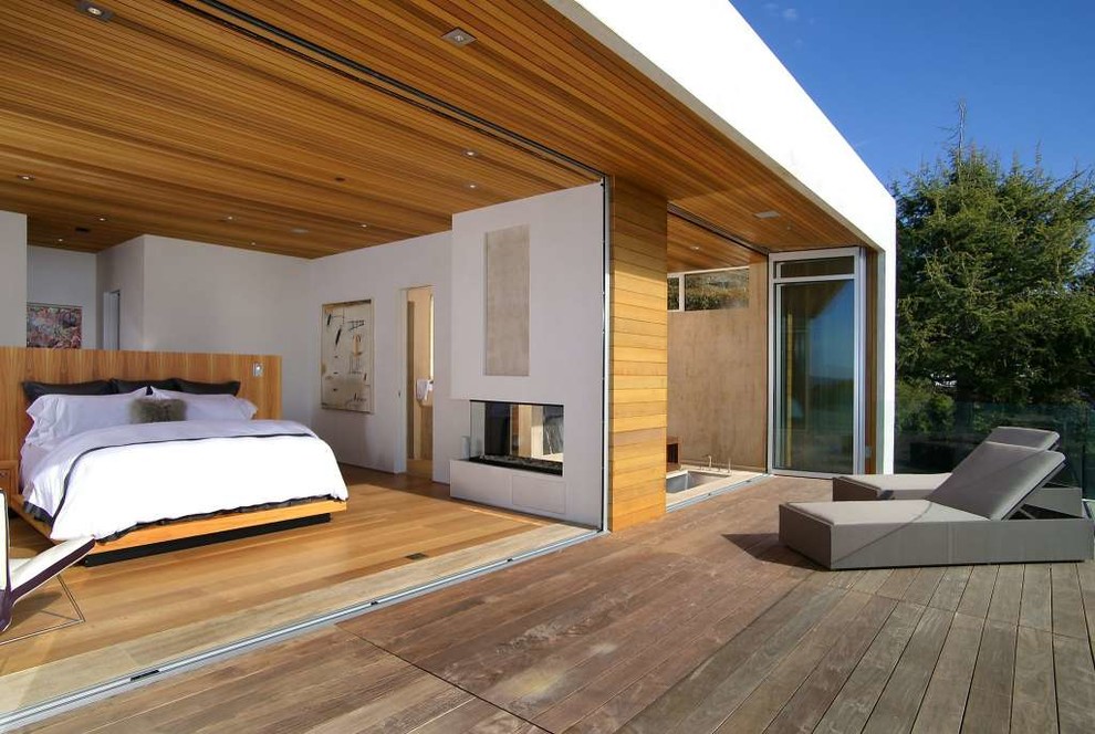 Geräumiges Modernes Schlafzimmer mit beiger Wandfarbe, Tunnelkamin, Kaminumrandung aus Stein und hellem Holzboden in San Francisco