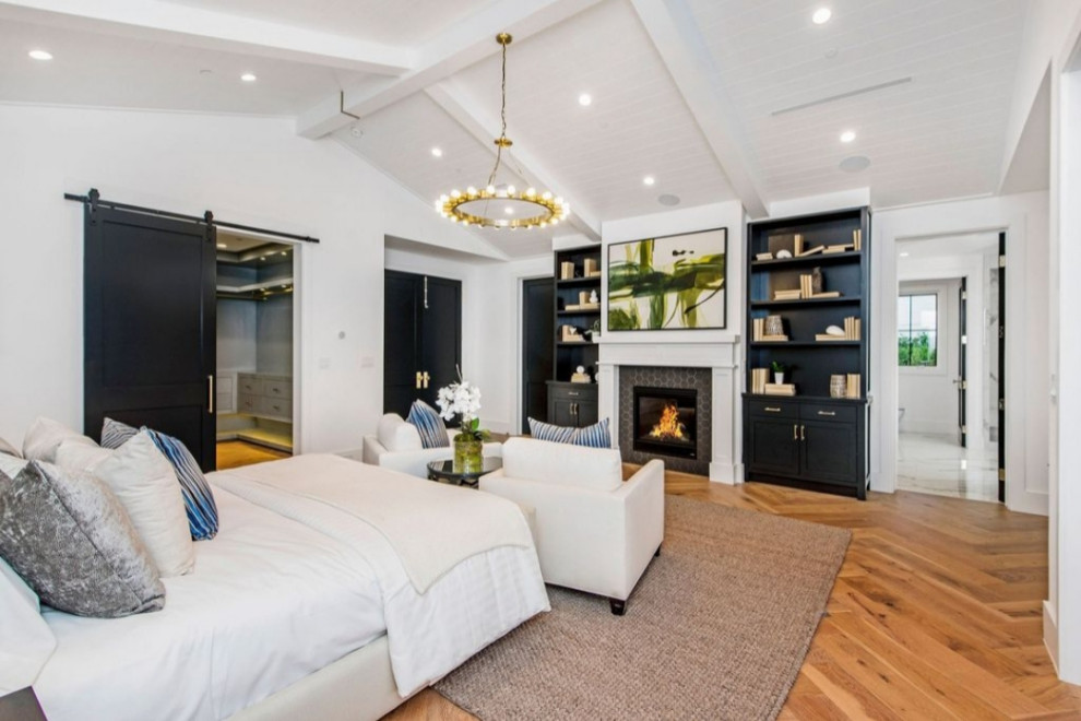 Geräumiges Landhaus Hauptschlafzimmer mit weißer Wandfarbe, hellem Holzboden, Kamin, Kaminumrandung aus Holz und braunem Boden in Los Angeles