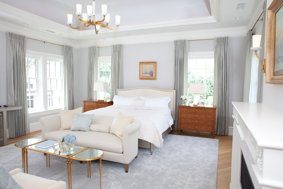 Foto de dormitorio clásico grande con suelo de madera clara, todas las chimeneas y marco de chimenea de piedra