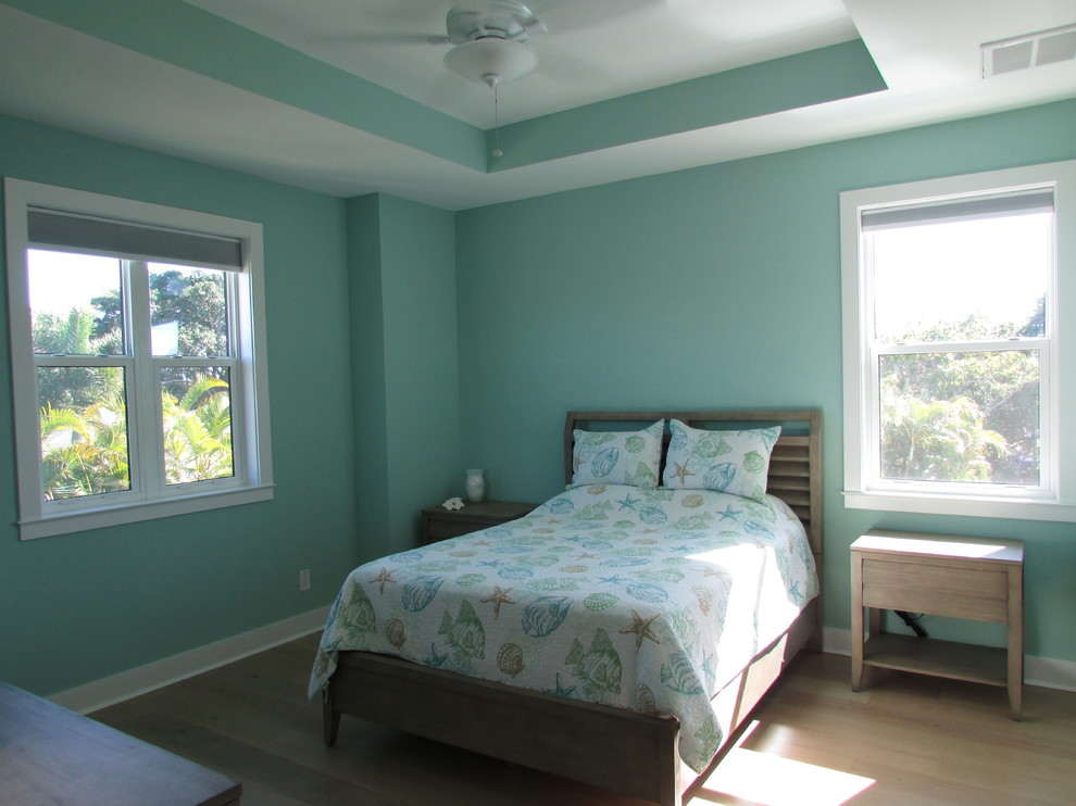Diseño de habitación de invitados costera de tamaño medio sin chimenea con paredes verdes, suelo de madera en tonos medios y suelo beige