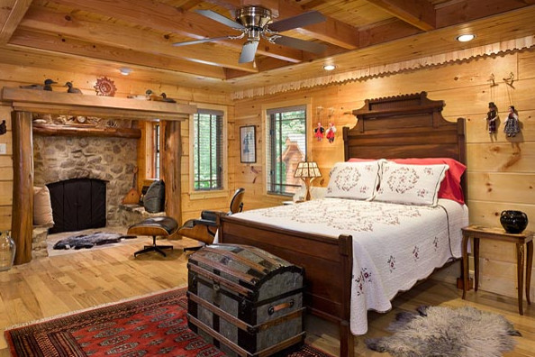 Großes Uriges Hauptschlafzimmer mit brauner Wandfarbe, braunem Holzboden, Kamin und Kaminumrandung aus Stein in Sonstige