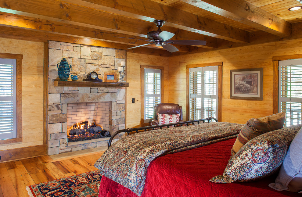 Großes Uriges Hauptschlafzimmer mit brauner Wandfarbe, braunem Holzboden, Kamin, Kaminumrandung aus Stein und braunem Boden in Sonstige
