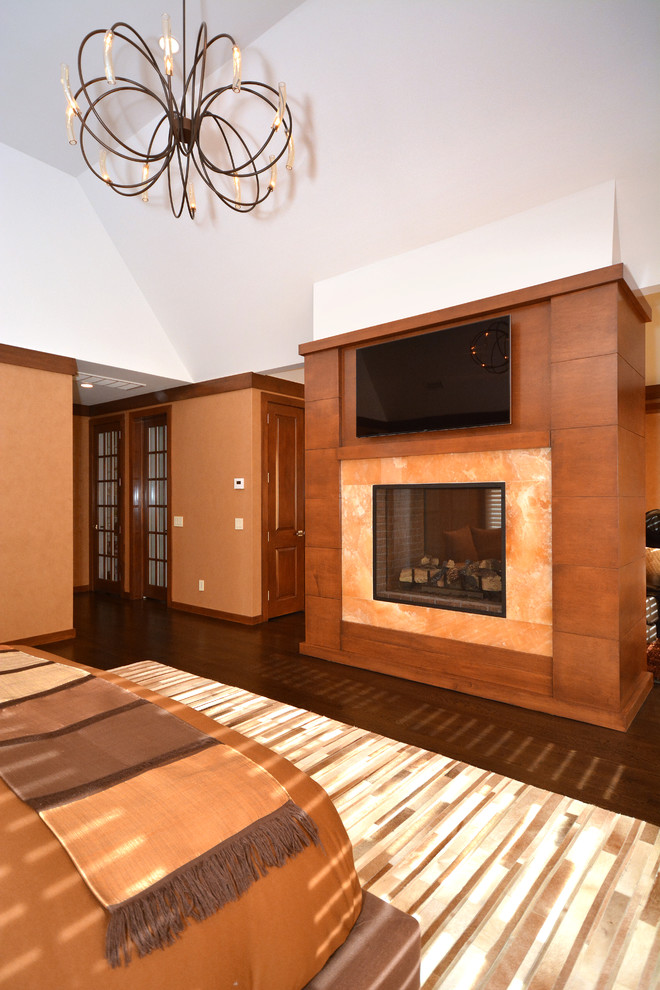 ニューヨークにある広いコンテンポラリースタイルのおしゃれな主寝室 (オレンジの壁、濃色無垢フローリング、両方向型暖炉、石材の暖炉まわり、茶色い床) のインテリア