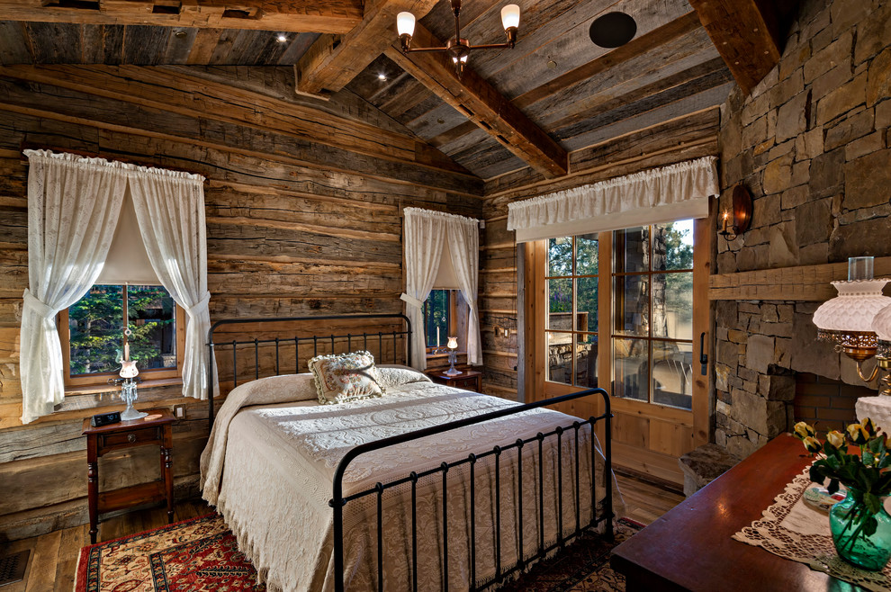 Example of a mountain style master dark wood floor bedroom design in Other with brown walls, a corner fireplace and a stone fireplace