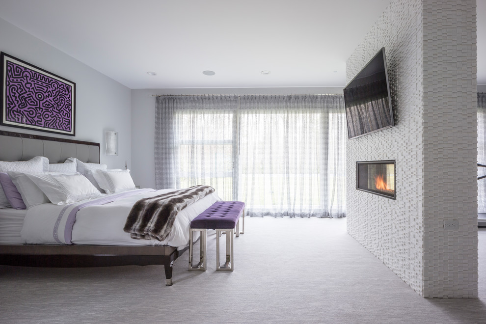 Immagine di una camera da letto bohémian con pareti bianche, moquette, camino bifacciale, cornice del camino in pietra e pavimento grigio