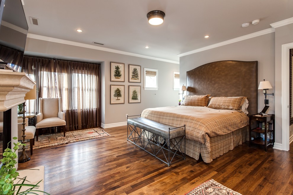 Cette photo montre une chambre parentale chic de taille moyenne avec un mur gris, un sol en bois brun et une cheminée standard.