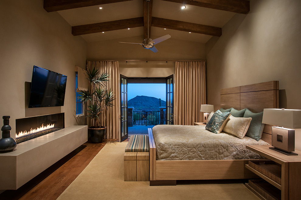 Modelo de dormitorio principal actual grande con paredes beige, suelo de madera en tonos medios, chimenea lineal y marco de chimenea de yeso