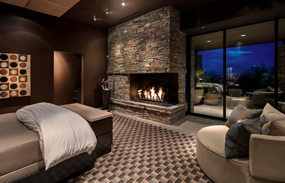 На фото: хозяйская спальня в современном стиле с коричневыми стенами, фасадом камина из камня и угловым камином