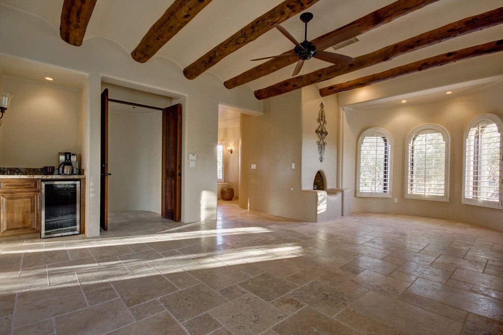 Cette photo montre une très grande chambre parentale sud-ouest américain avec un mur beige, un sol en travertin, une cheminée standard et un manteau de cheminée en plâtre.