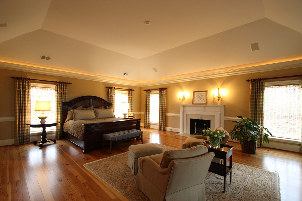 Réalisation d'une chambre tradition avec un mur beige, un sol en bois brun, une cheminée standard et un manteau de cheminée en pierre.