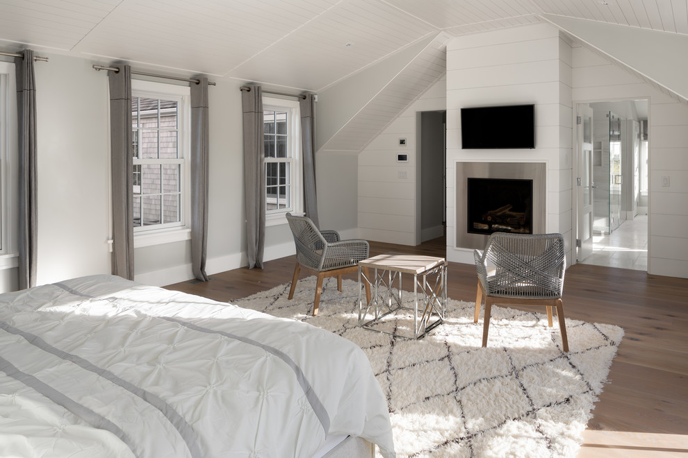 Design ideas for a large beach style master bedroom in Boston with grey walls, light hardwood flooring, a hanging fireplace and a metal fireplace surround.