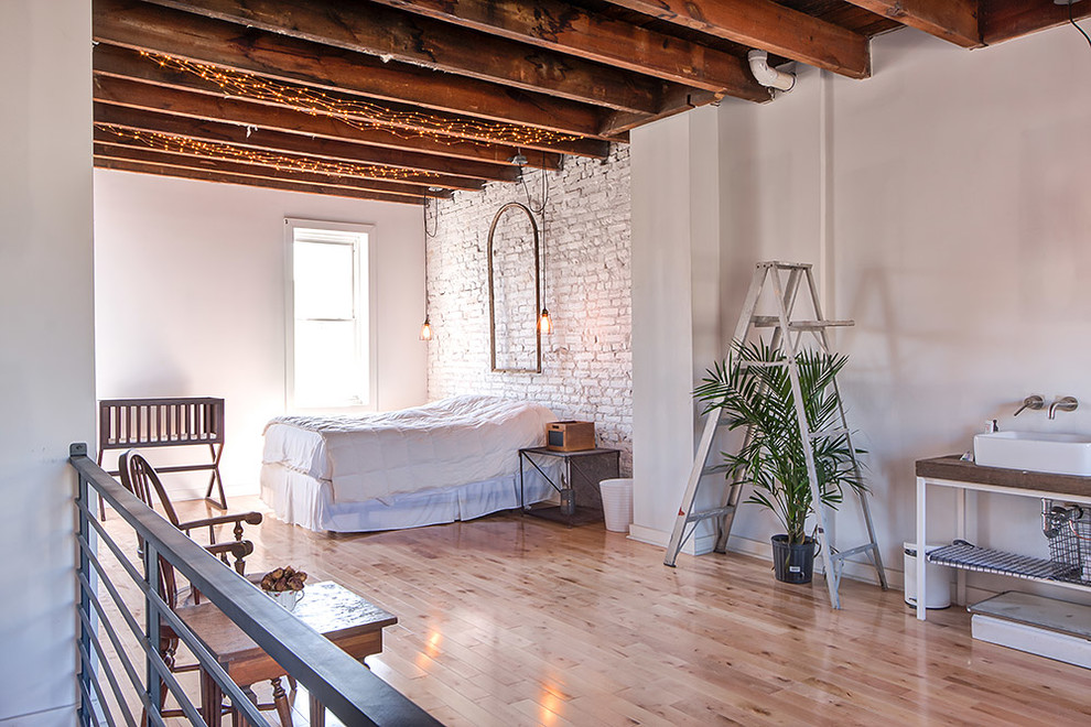 Ejemplo de dormitorio tipo loft industrial grande con paredes blancas y suelo de madera clara