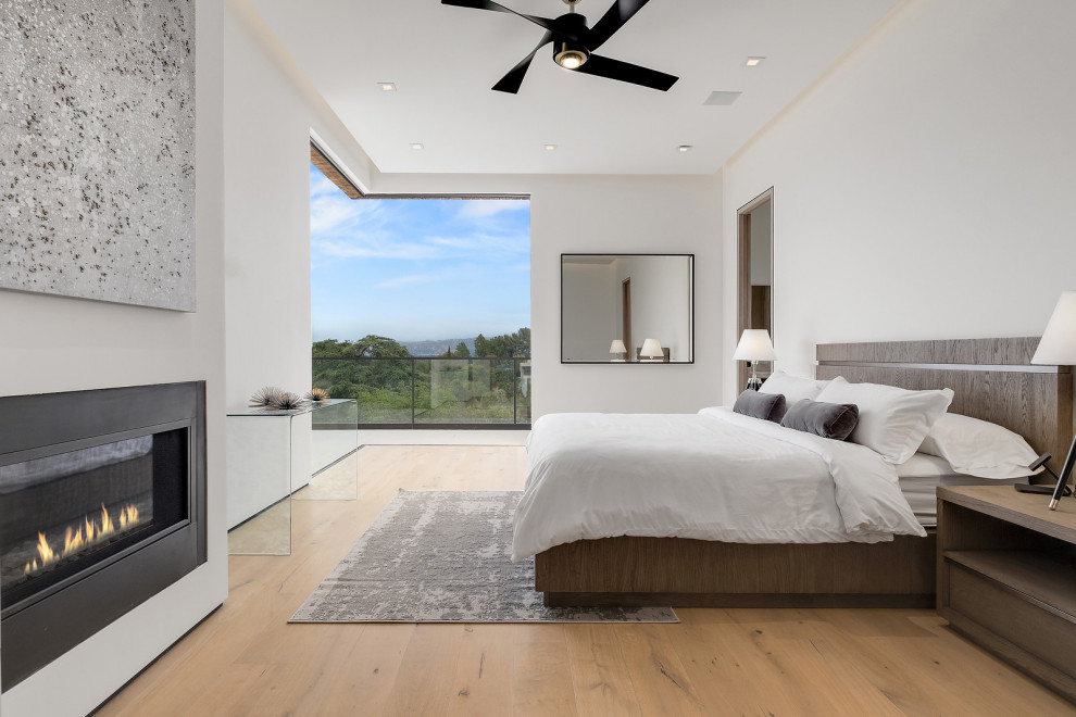 Ejemplo de dormitorio principal contemporáneo grande con paredes blancas, suelo de madera en tonos medios, chimenea lineal y suelo marrón
