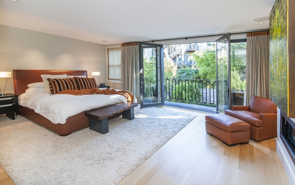 На фото: большая хозяйская спальня в стиле модернизм с серыми стенами, светлым паркетным полом, горизонтальным камином и фасадом камина из штукатурки с