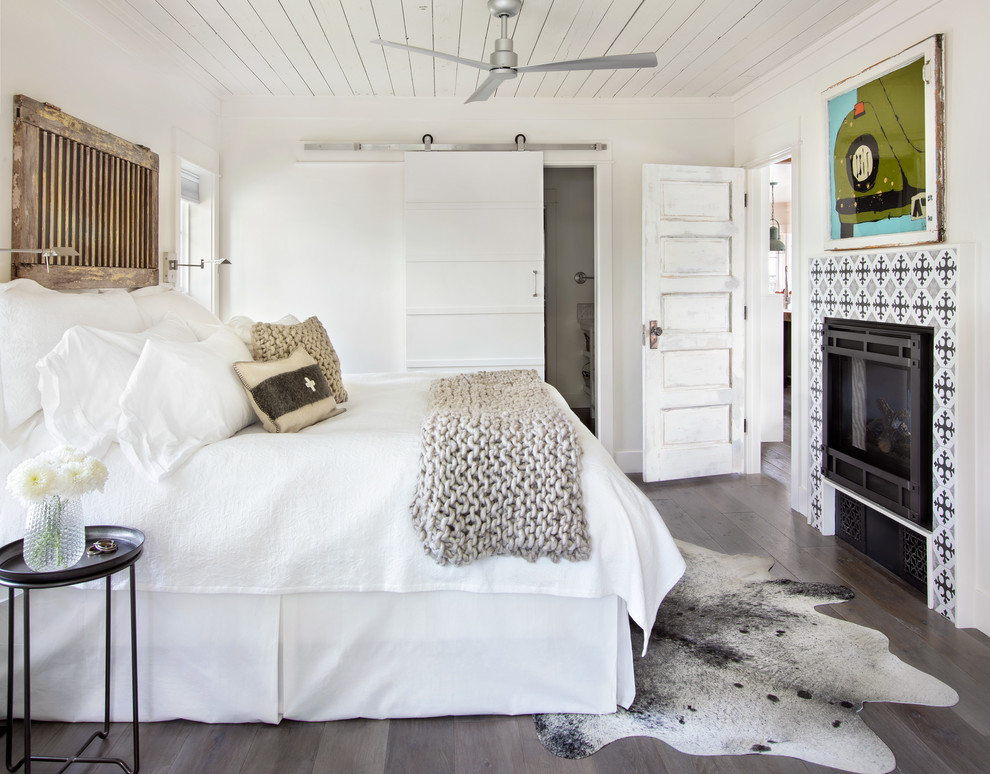 Imagen de dormitorio campestre con paredes blancas, suelo de madera oscura, marco de chimenea de baldosas y/o azulejos, chimenea lineal y suelo marrón