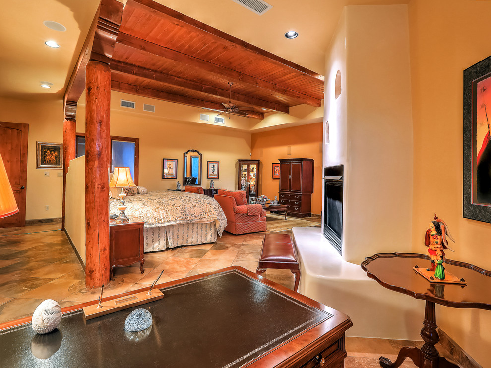 Cette image montre une chambre parentale sud-ouest américain de taille moyenne avec un mur jaune, un sol en ardoise, une cheminée standard, un manteau de cheminée en plâtre et un sol multicolore.